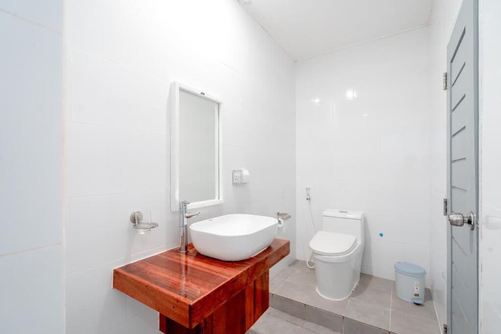 A modern bathroom with a wooden vanity, a white sink, a toilet, and a trash bin.
