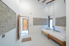 A bedroom with a bed, a wooden bench, and a brick accent wall. - Brickwood Shoreline (Rasdhoo)