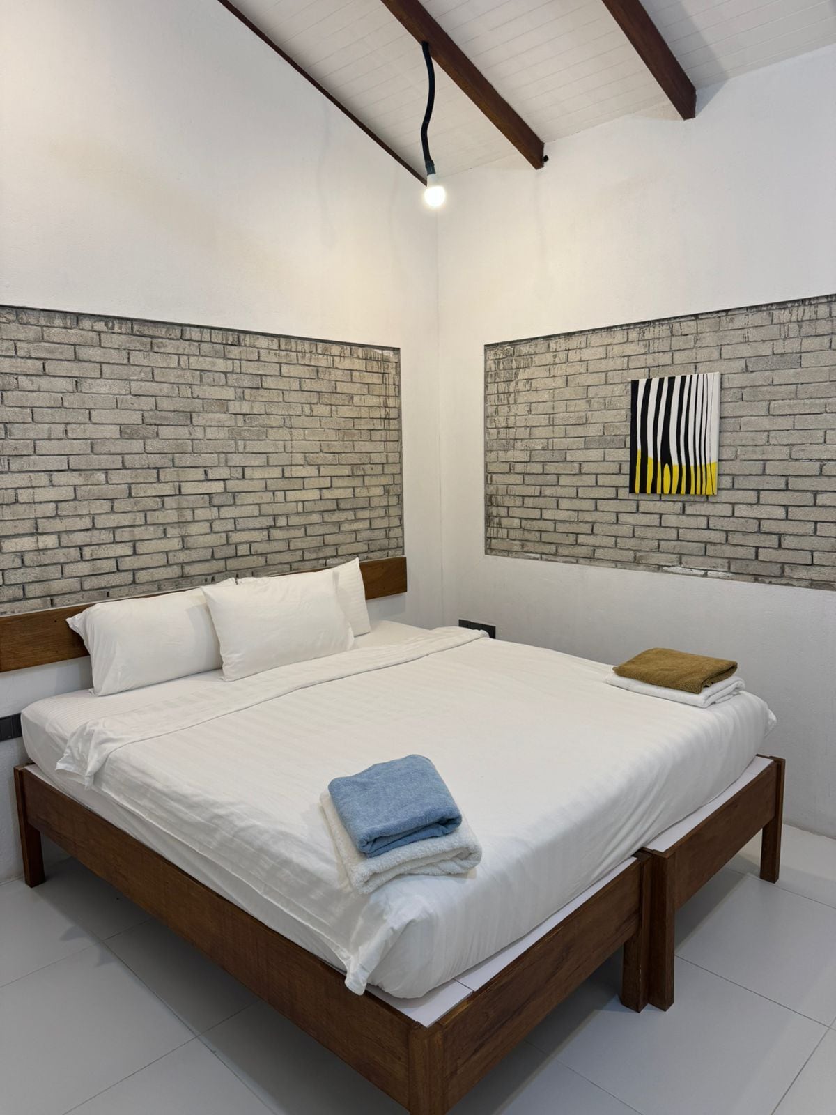Une chambre avec une tête de lit ornée d’un motif en briques, un lit recouvert de linge de maison blanc et une seule œuvre d’art accrochée au mur.