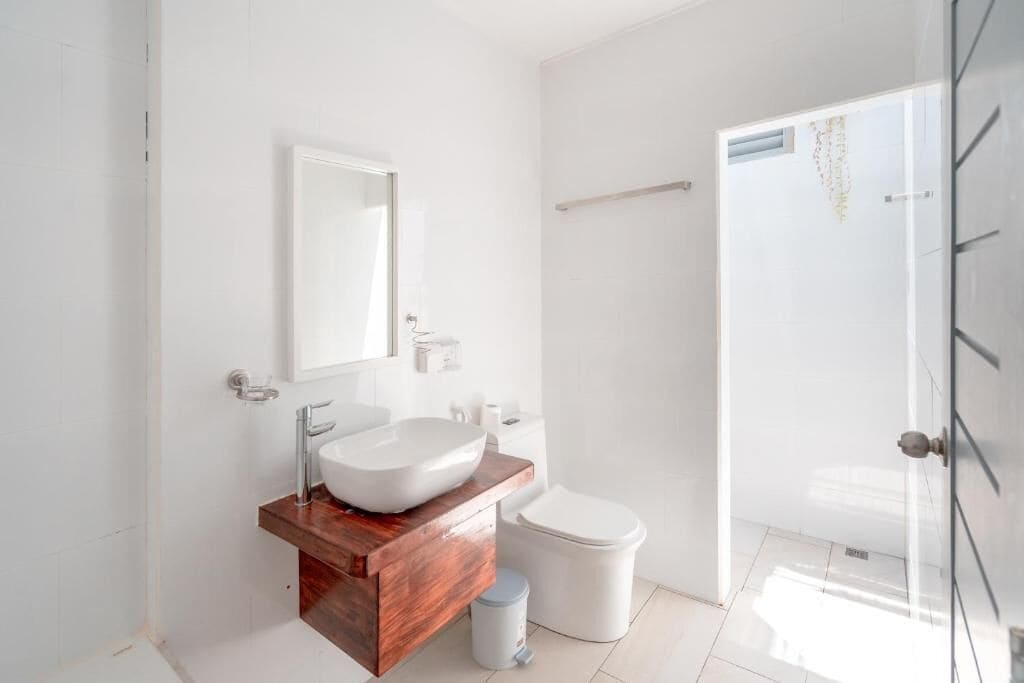 A modern bathroom with a wooden vanity, a white sink, a toilet, and a glass shower enclosure.