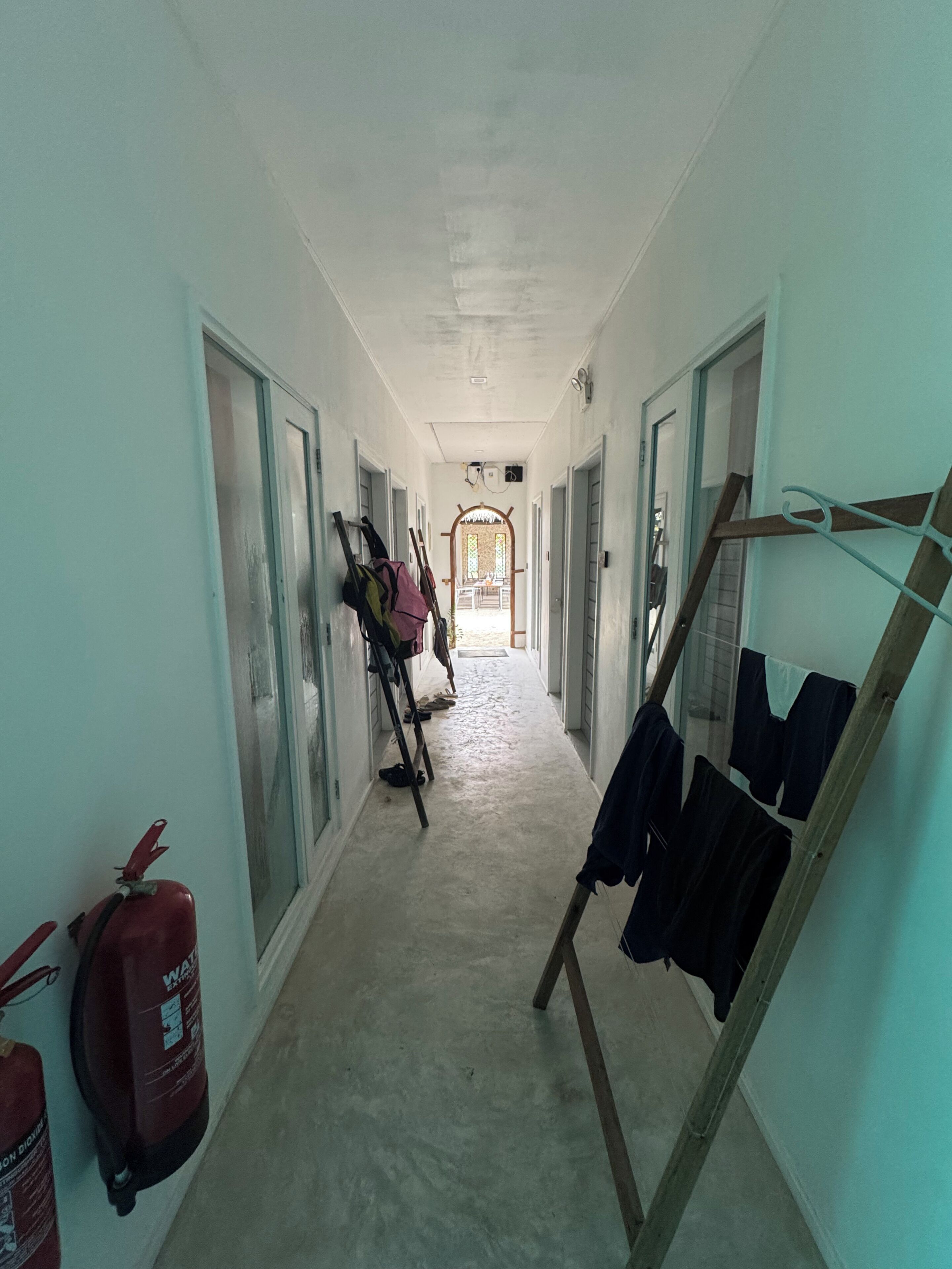 Un pasillo con puertas a ambos lados, un extintor y un tendedero.