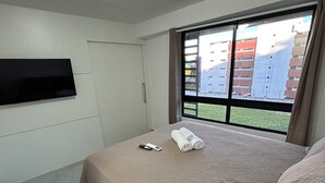 Une chambre d’hôtel moderne dotée d’un grand lit, d’un téléviseur à écran plat fixé au mur et d’une fenêtre donnant sur des immeubles.