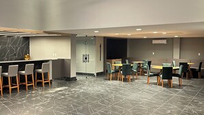 Moderni hotellin aula, jossa on marmorilattia, baaritiski jakkaroineen sekä oleskelualue pyöreine pöytineen ja tuoleineen.