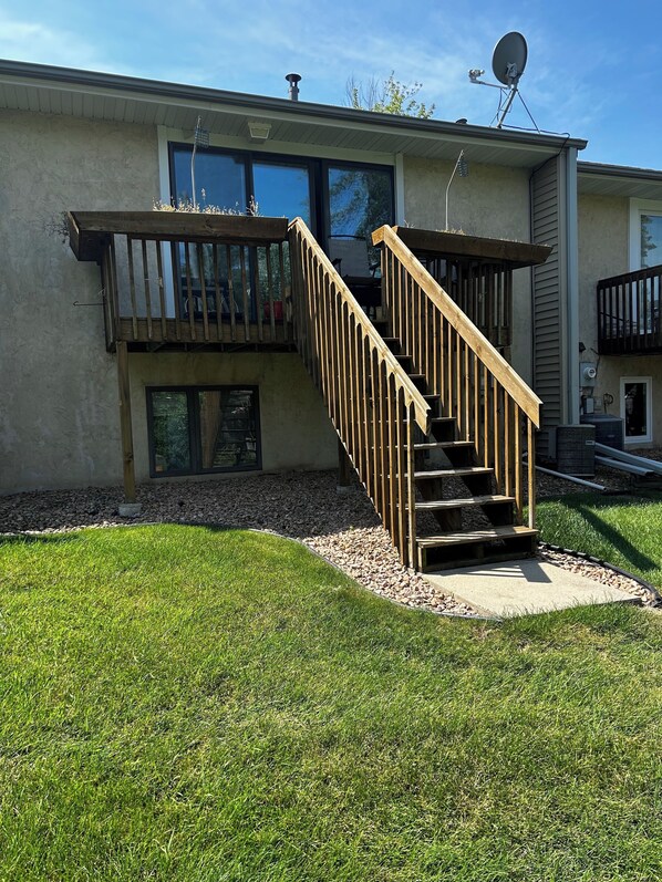 A residential building with a wooden staircase leading to a balcony, a satellite dish, and a clear sky.