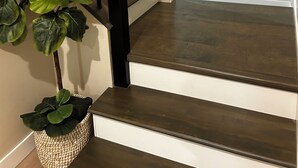 A staircase with dark wooden steps and a black handrail, leading to a landing with a light switch.