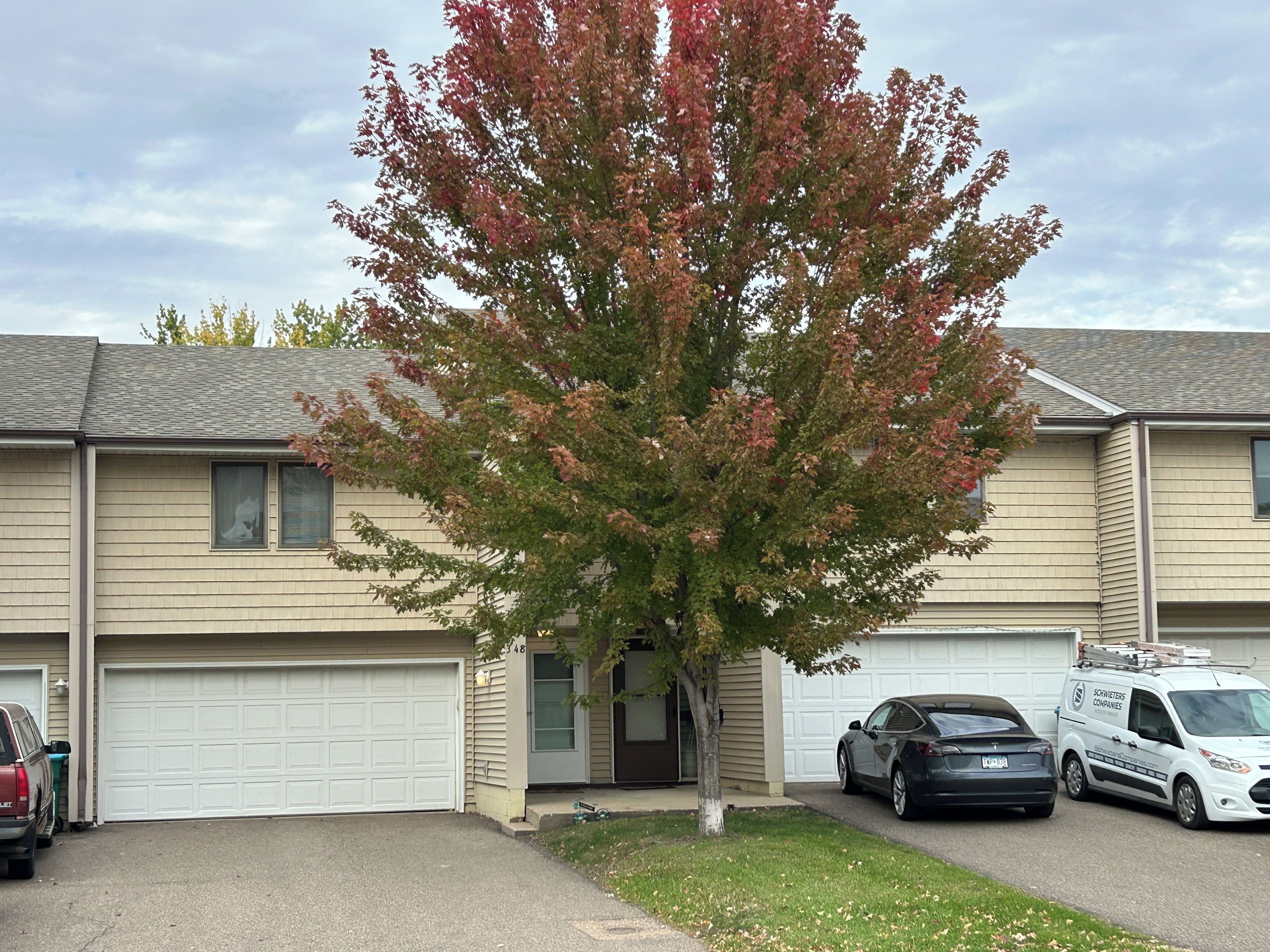 A residential building with a garage, a driveway, and a tree in front.