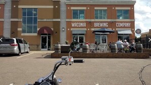 A building with a sign reading "Waconia Brewing Company" and a parking lot with a motorcycle in the foreground.