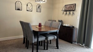 A dining area with a round table, patterned chairs, a red vase, and wall art.