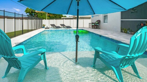 A swimming pool with two turquoise chairs and a blue umbrella. - 5 Star, 3 bd Home, Heated Pool Located D-town Cape (Cape Coral)