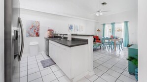 A modern kitchen with white cabinets, a stainless steel refrigerator, and a dining area with a table and chairs. - 5 Star, 3 bd Home, Heated Pool Located D-town Cape (Cape Coral)