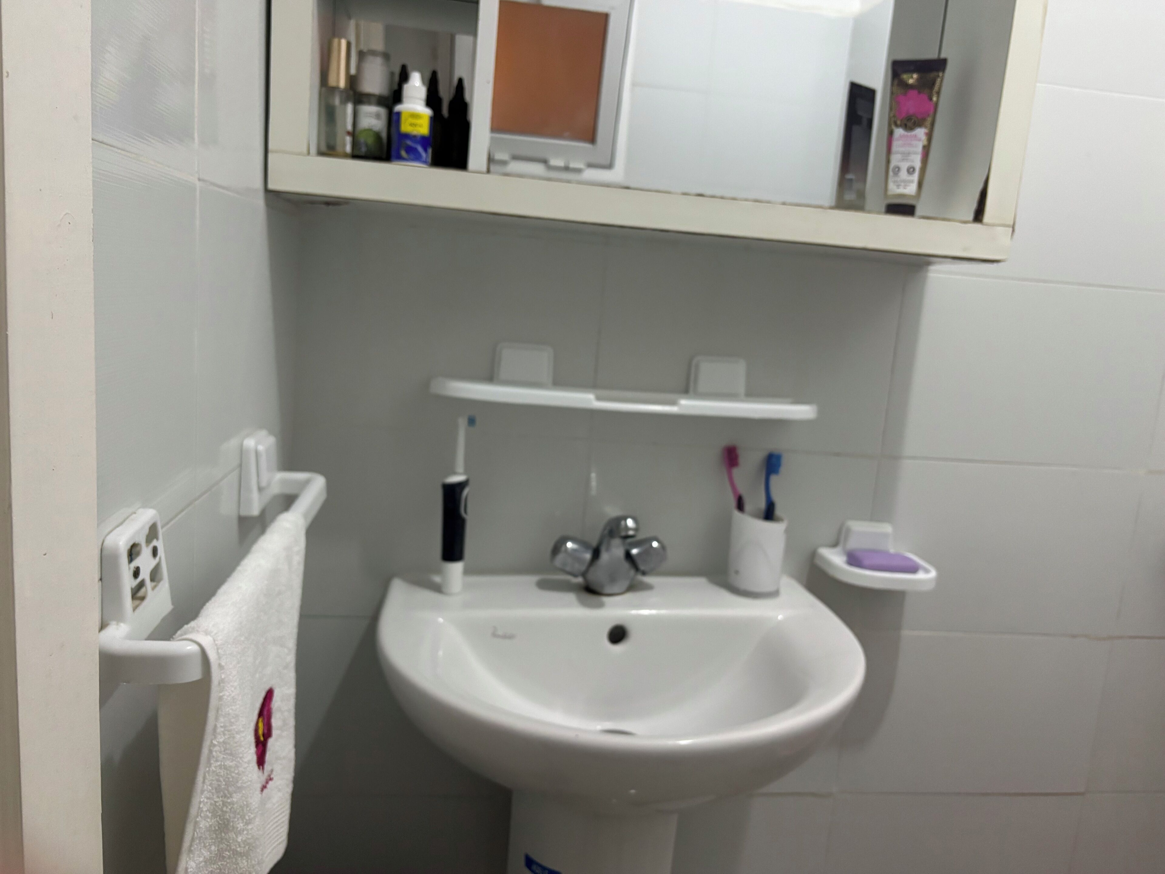 Un baño con lavamanos blanco, toallero con toalla, porta cepillos de dientes y jabonera.