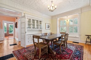 Una sala da pranzo con tavolo e sedie in legno, un tappeto decorato e vista sull'esterno tramite ampie finestre.