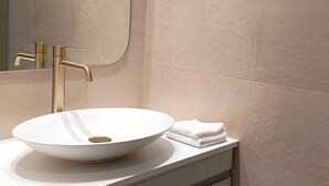 Een badkamer met een wit wastafel, een gouden kraan en een spiegel.