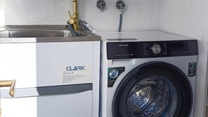 Een praktische keuken met een spoelbak, een compacte was-droogcombinatie en een klein aanrecht.