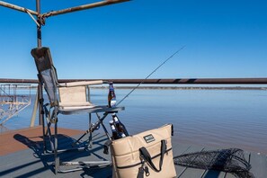 A fishing chair, a bag, and a fishing rod on a dock with calm water and a clear sky.