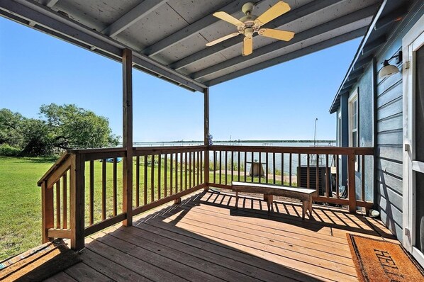 A wooden deck with a ceiling fan, a bench, and a view of a grassy area.