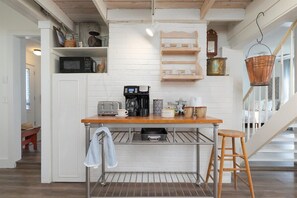 Une cuisine avec un plan de travail en bois, une machine à café, un grille-pain et un seau en cuivre suspendu.