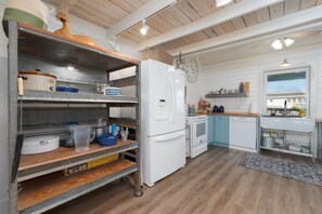 Een keuken met een witte koelkast, houten planken, een fornuis en een klok aan de muur.