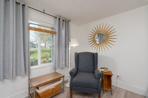 A room with a window, a chair, a lamp, and a wall-mounted mirror.