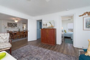 Een ruime woonkamer met een eettafel, een bank, een houten kast en een gang naar een slaapkamer.