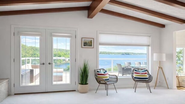 A spacious room with a large window overlooking a body of water, a door leading to an outdoor area, and a potted plant.