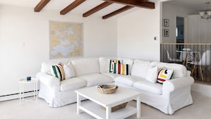 A white sectional sofa with colorful pillows, a white coffee table, and a world map on the wall.