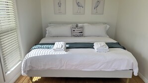 A neatly made bed with white linens, a pillow with 'The Lake House' text, and three wall-mounted bird paintings.