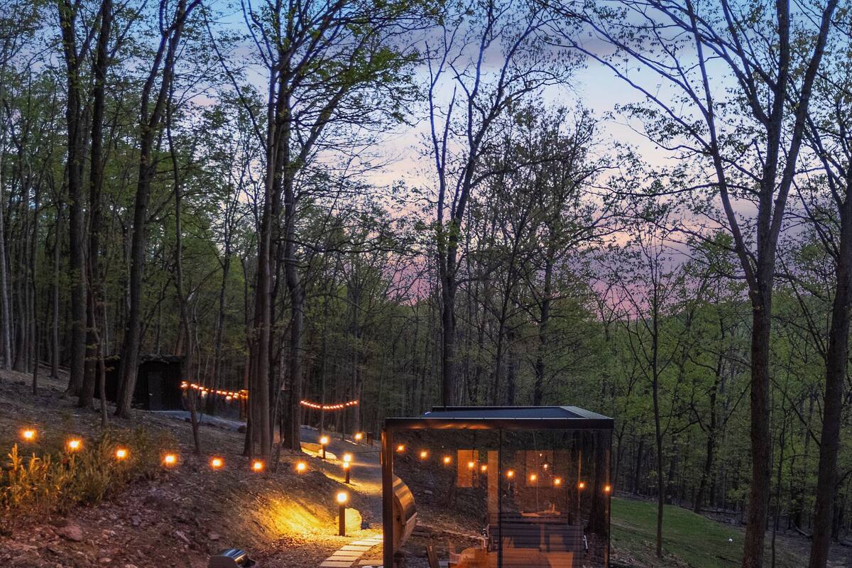 Una cabaña rústica con cerramiento de vidrio, un jacuzzi y una terraza de madera con luces colgantes.