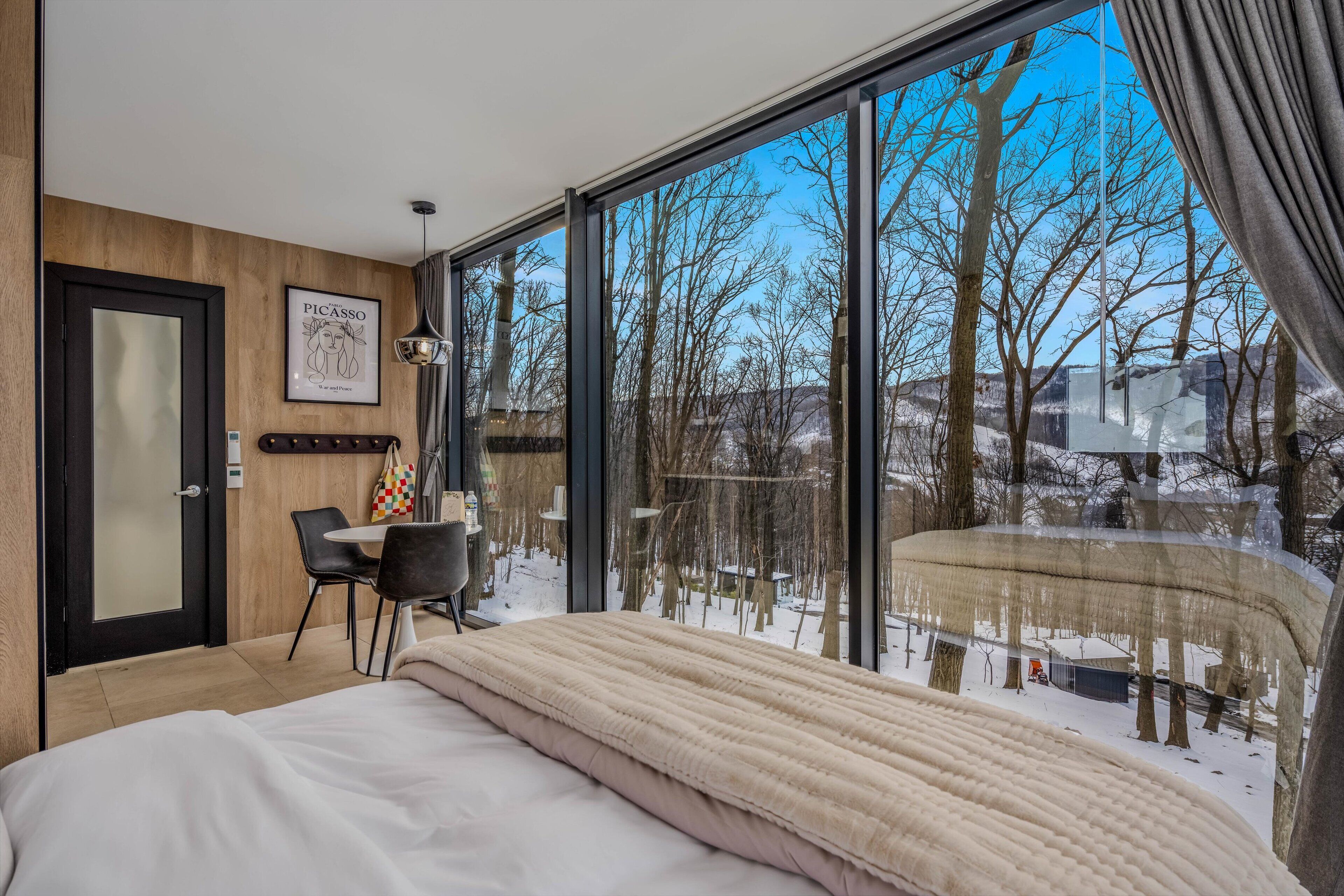 A modern bedroom with a large window, a bed, a desk, and a chair.