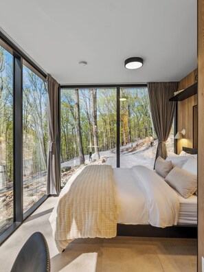 A modern bedroom with a large bed, a view of a forest through floor-to-ceiling windows, and a minimalist design. - Mirror Villas - Modern Retreat with private hot tubs and mountain view (Mercersburg)