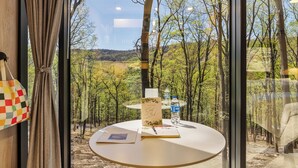 A room with a round table, two chairs, a hanging light fixture, and a view of a forest through large windows. - Mirror Villas - Modern Retreat with private hot tubs and mountain view (Mercersburg)