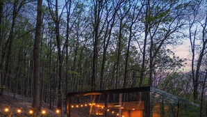 A glass-enclosed cabin with a fire pit, outdoor seating, and string lights in a forested area. - Mirror Villas - Modern Retreat with private hot tubs and mountain view (Mercersburg)