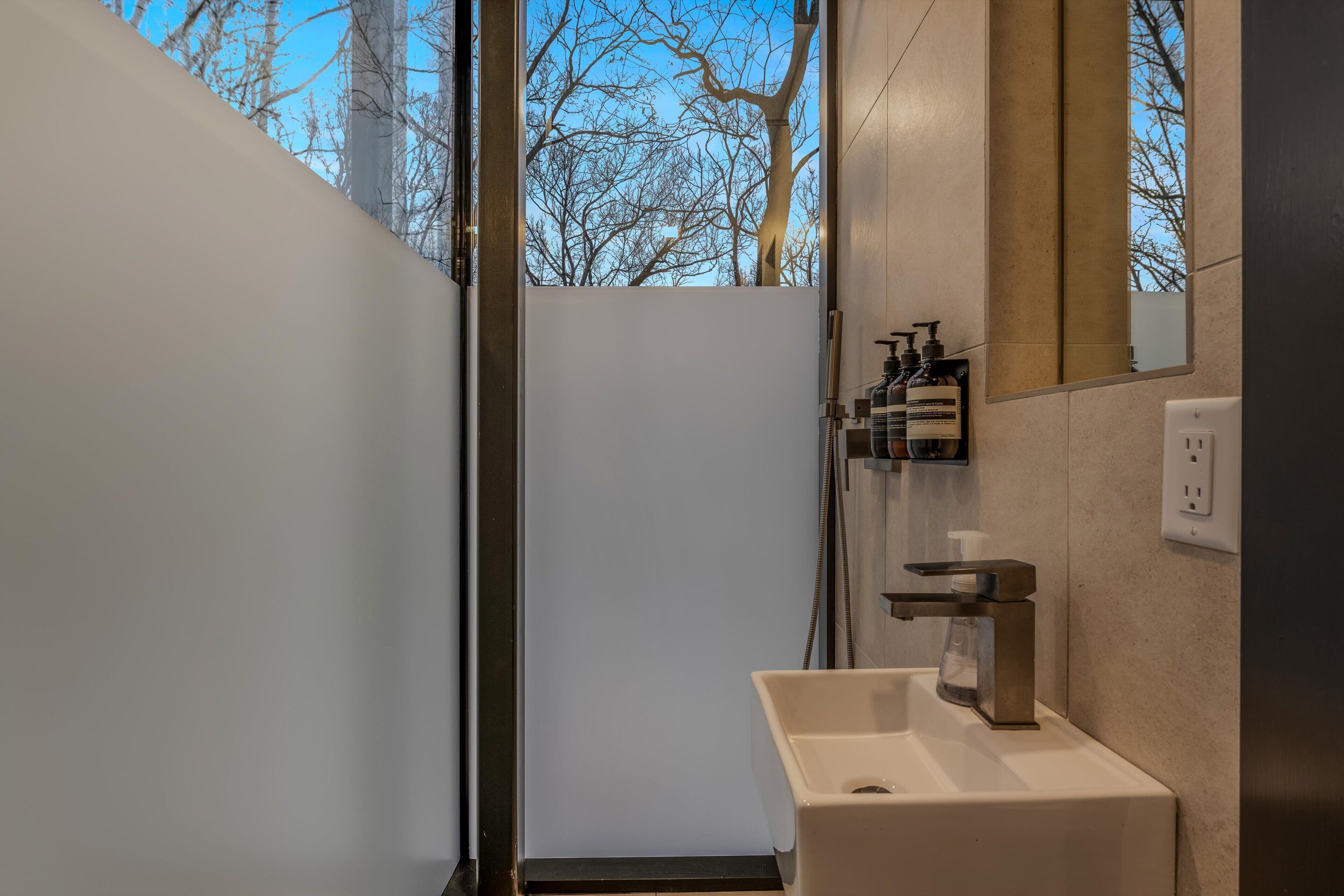 Un baño moderno con lavamanos blanco, espejo y artículos de aseo en una repisa.