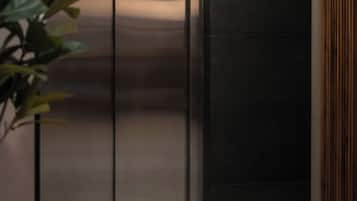 Un elevador moderno con detalles metálicos, piso de mármol y una planta en su izquierda.
