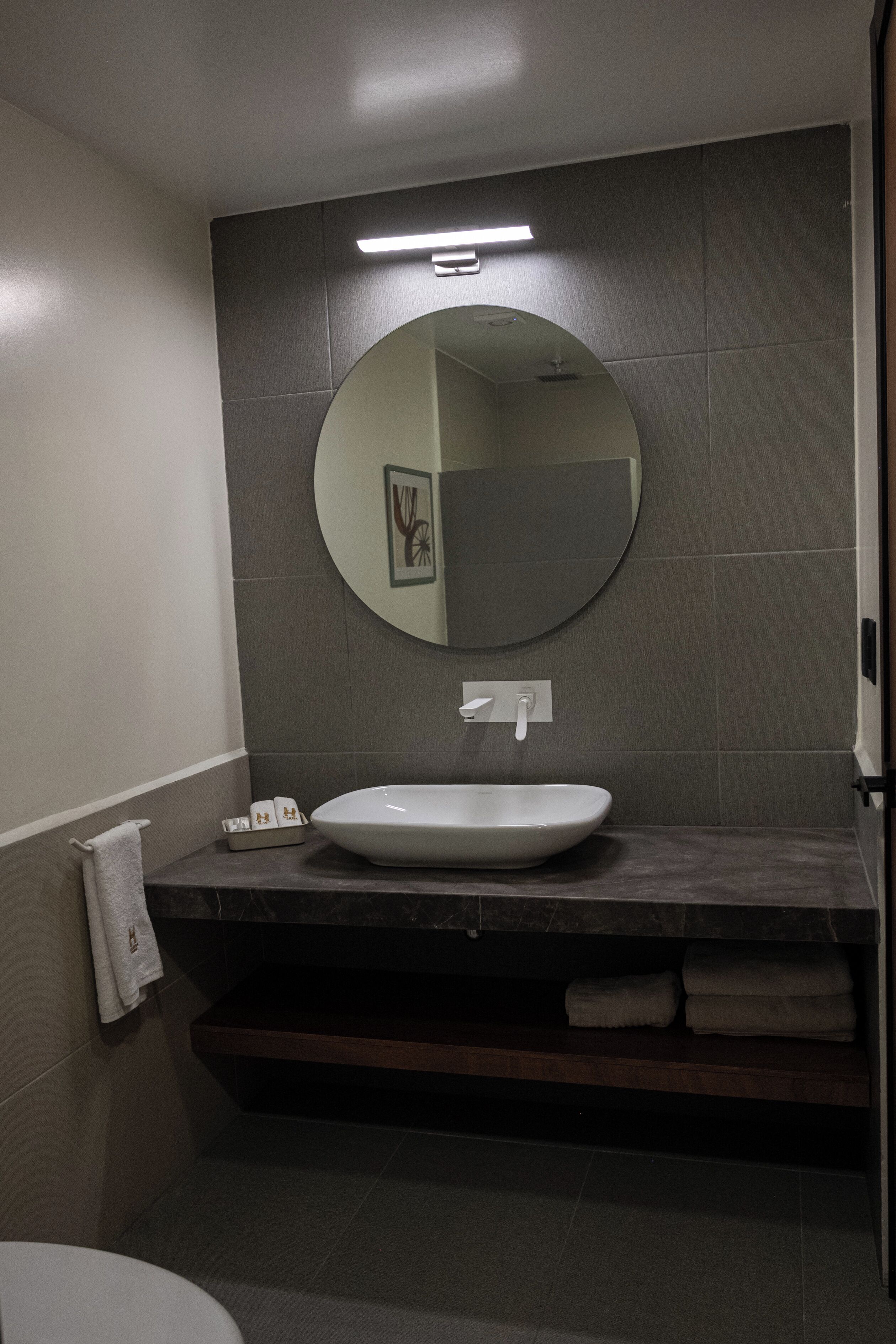 A bathroom with a round mirror, a white sink, and a towel rack.