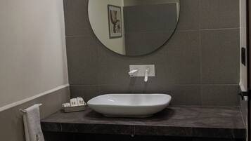 Un baño con un espejo redondo, un lavabo blanco y un perchero para toallas.