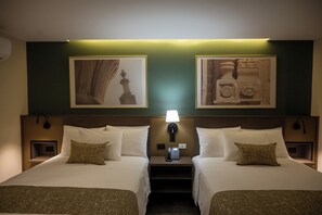 A hotel room with two beds, a nightstand with a lamp, and framed artwork on the wall. - Hilaria (Aguascalientes)