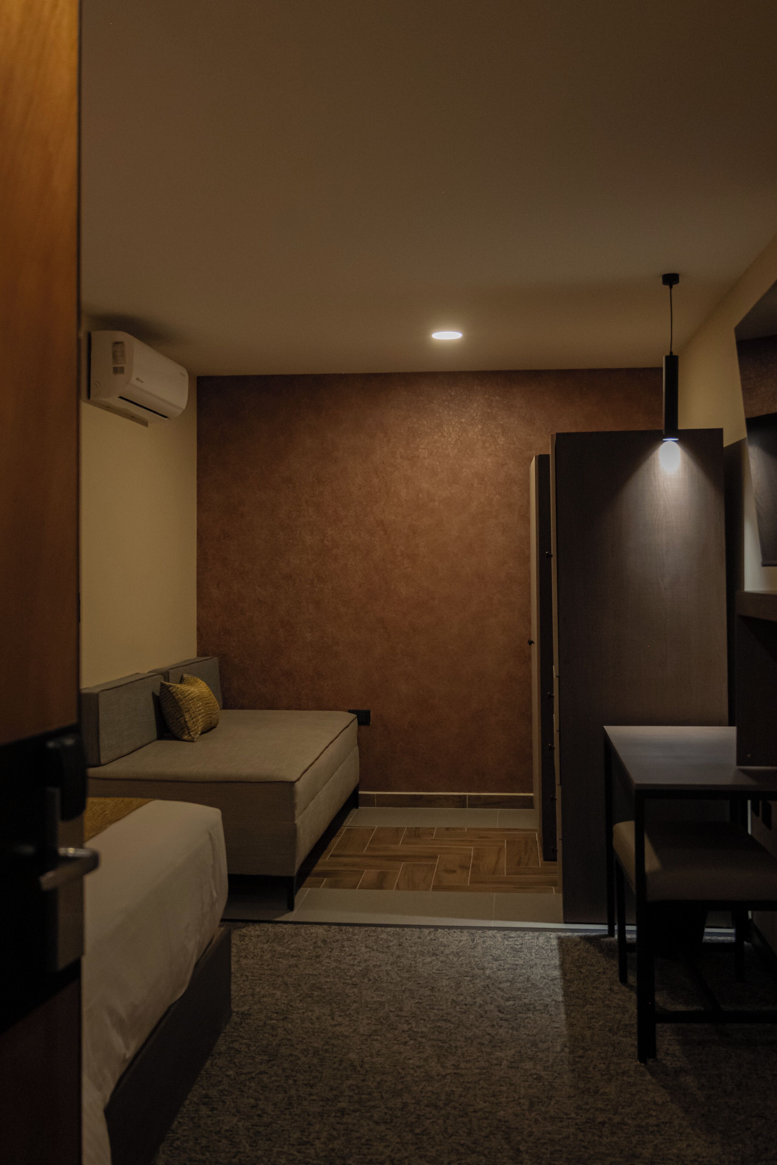 A compact hotel room with a bed, a small sofa, a desk, and a chair.