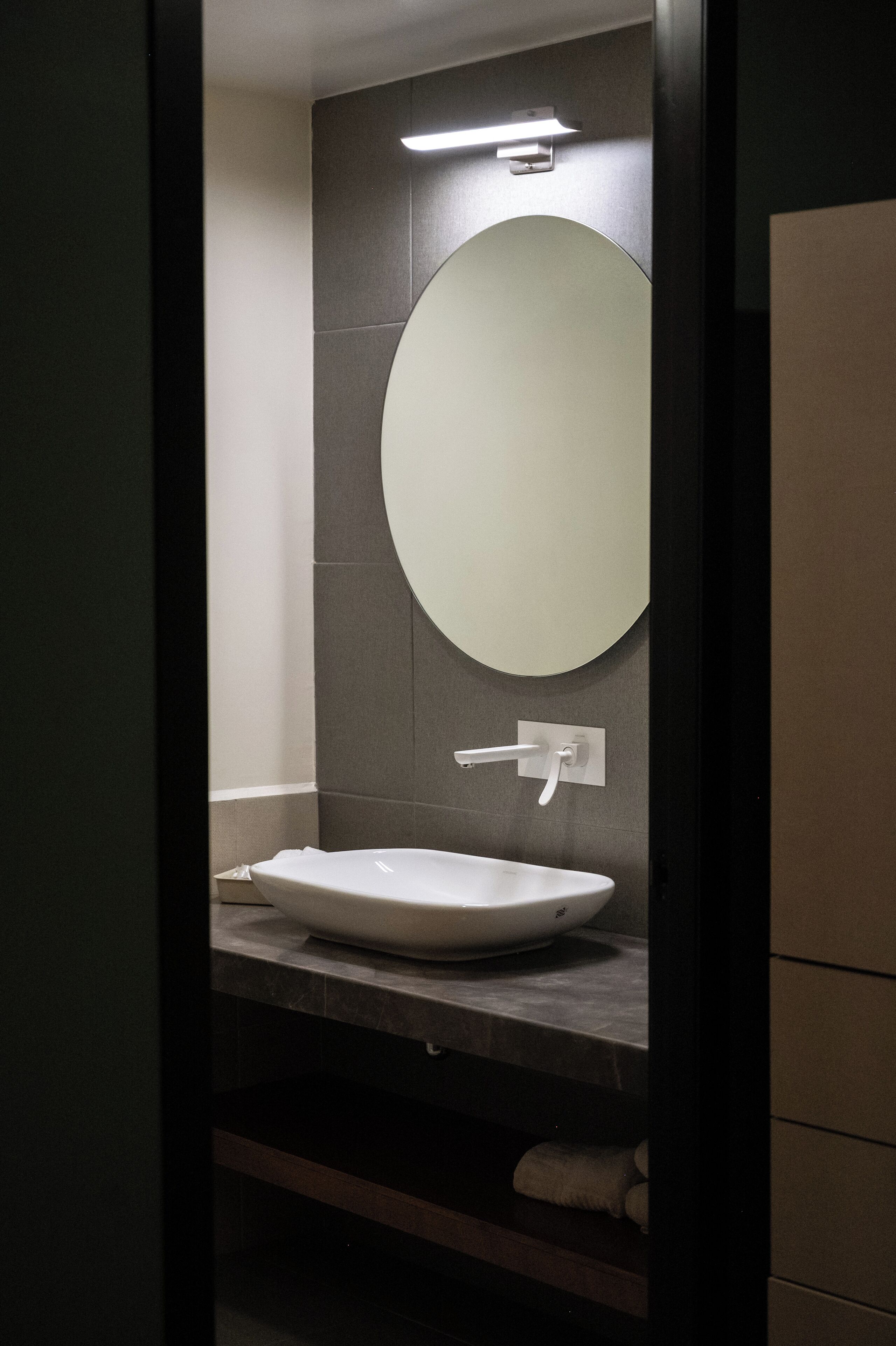 Een moderne badkamer met een ronde spiegel, een witte wastafel en een handdoekhouder.