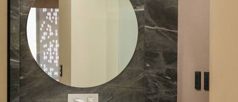Une salle de bain avec un miroir rond, un lavabo blanc et un porte-serviettes.