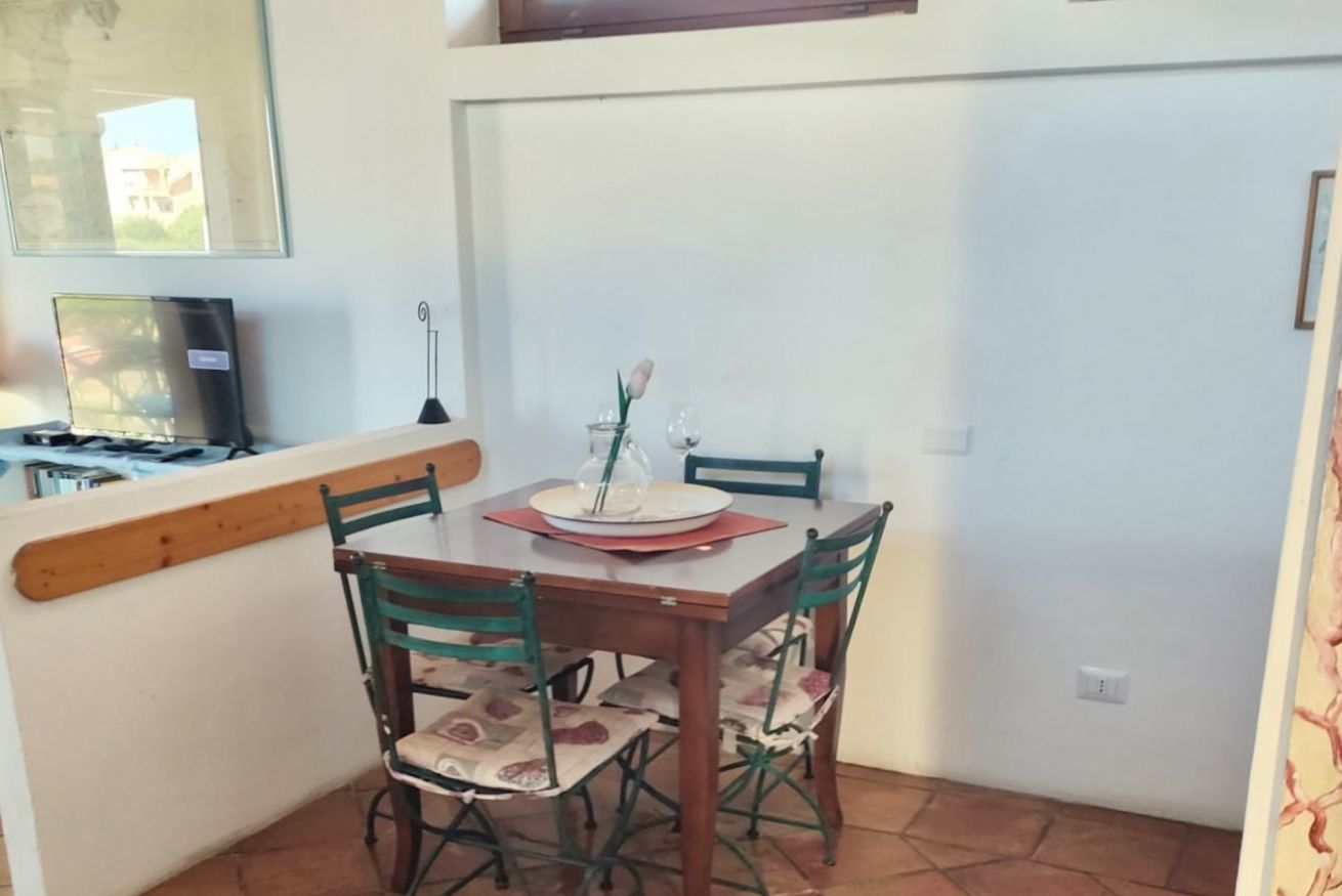 Een eetgedeelte met een houten tafel en stoelen, een kleine vaas met één bloem, en een laptop op de tafel.