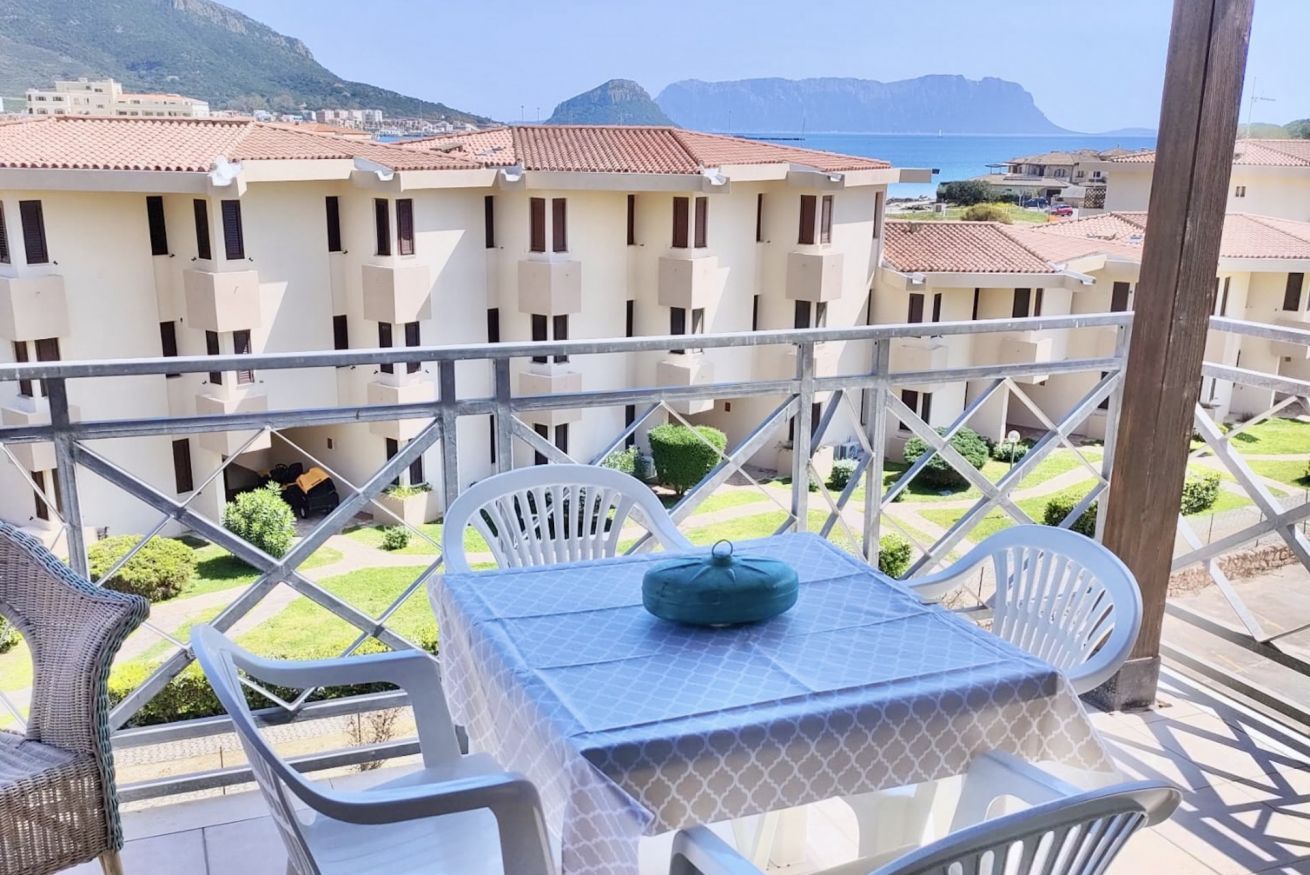 Un balcon avec une table et des chaises, donnant sur un quartier résidentiel avec des immeubles et offrant une vue sur la mer.