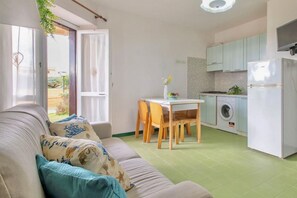 A compact living space with a sofa, a dining table, and a kitchen area including a washing machine and a refrigerator.
