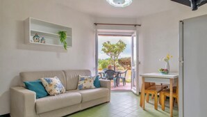 Un salon comprenant un canapé, une petite table et un fauteuil. Une porte donne accès à un espace extérieur aménagé avec une table et des chaises.