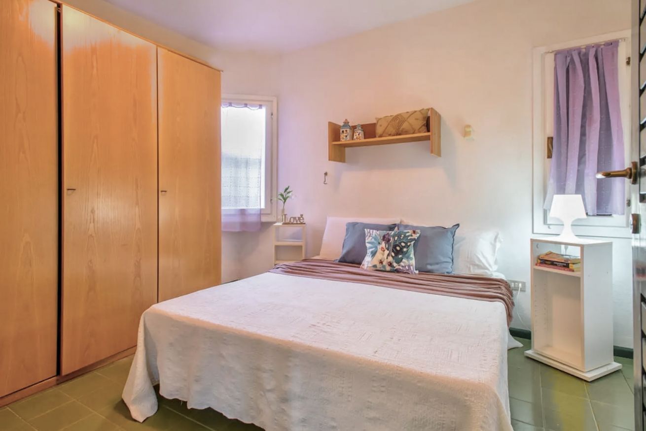 Ein Schlafzimmer mit Bett, Kleiderschrank, Nachttisch mit Lampe und einer Regal mit Dekoration.