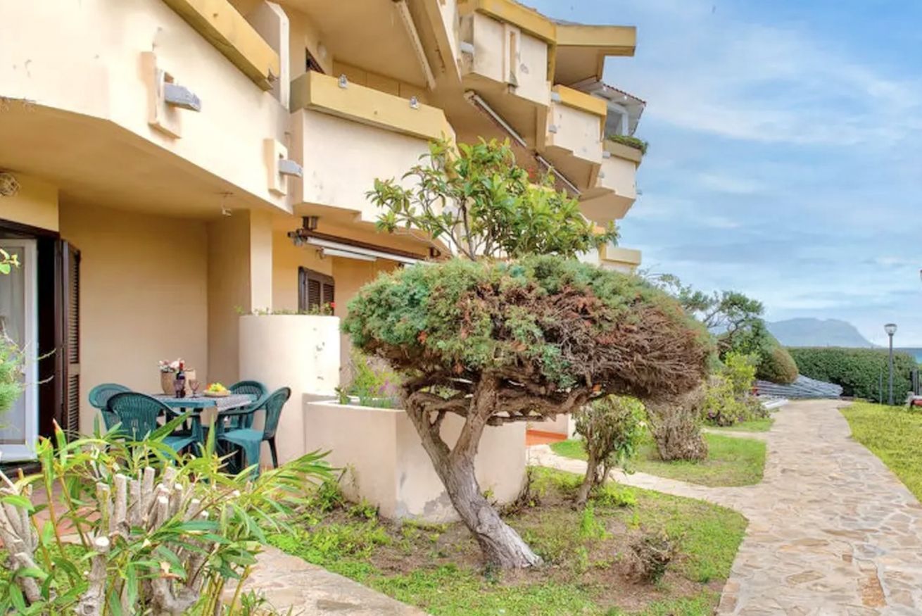 Un bâtiment avec un chemin en pierre, une petite table entourée de chaises et un jardin bien entretenu, agrémenté d’un arbre remarquable.