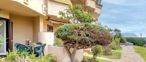 A building with a stone pathway, a small table with chairs, and a well-maintained garden with a unique tree.
