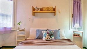 Une chambre à coucher bien rangée, avec un lit, des oreillers, une table de chevet, une étagère avec des objets décoratifs et une fenêtre avec un rideau.
