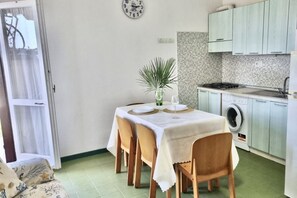 A dining area with a table set for four, a washing machine, and a kitchen with light-colored cabinets.