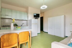 A modern kitchen with green cabinets, a white countertop, and a dining area with two wooden chairs.